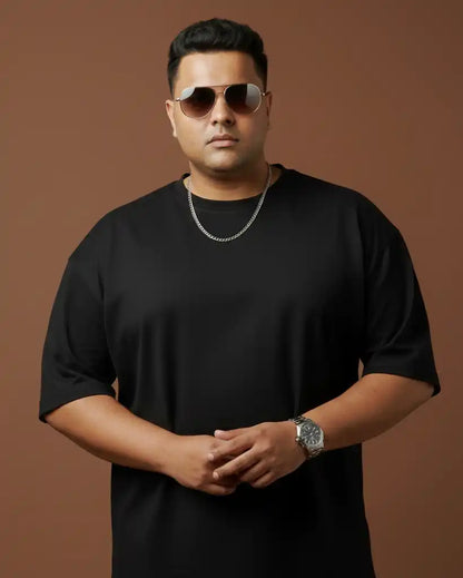 Plus size black oversized t-shirt on plus size male model wearing chain necklace and sunglasses, arms crossed front view against brown background, premium AWBlack plain tee