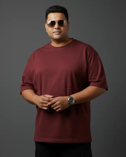 Plus size maroon oversized t-shirt on plus size male model wearing sunglasses, arms crossed front view against gray background, premium AWBlack plain tee