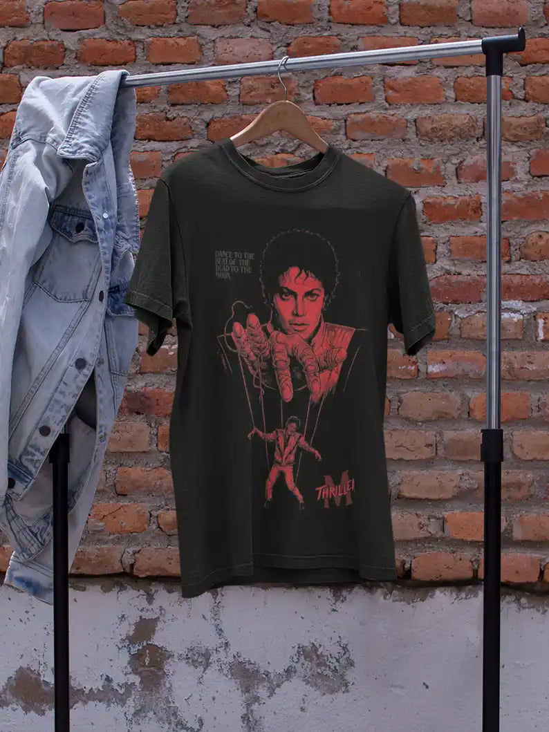 AWBlack Michael Jackson Thriller Vintage Music Puppet Graphic T-Shirt in Olive Green hanging on wooden hanger with denim jacket | Premium 180 GSM Cotton | Multi-Fit Regular, Oversized & Plus Size S–7XL | Red Thriller Print Streetwear Tee for Men | Rustic Brick Wall Background